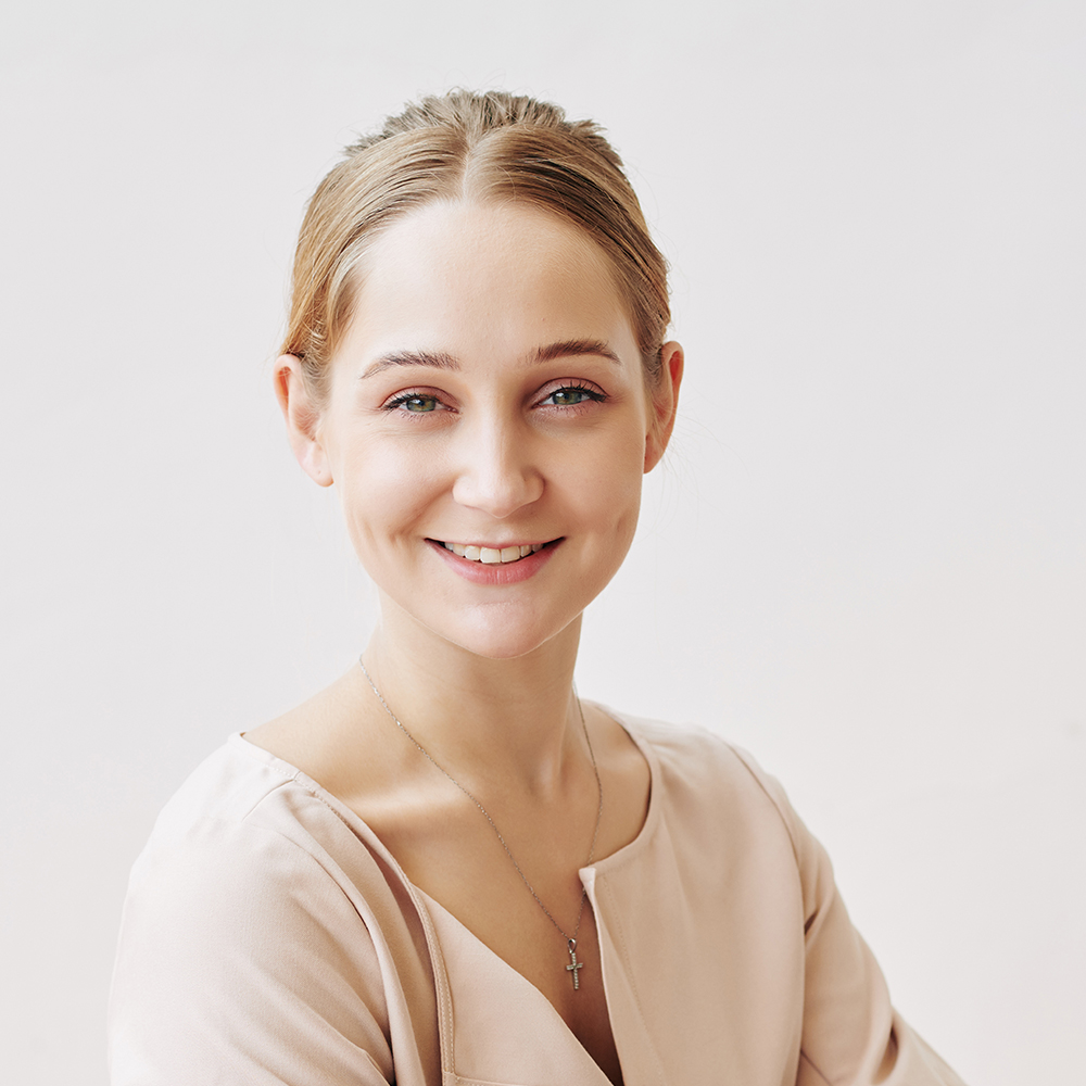 Vertical portrait of cheerful young woman sitting at office table working on laptop looking at camera smiling